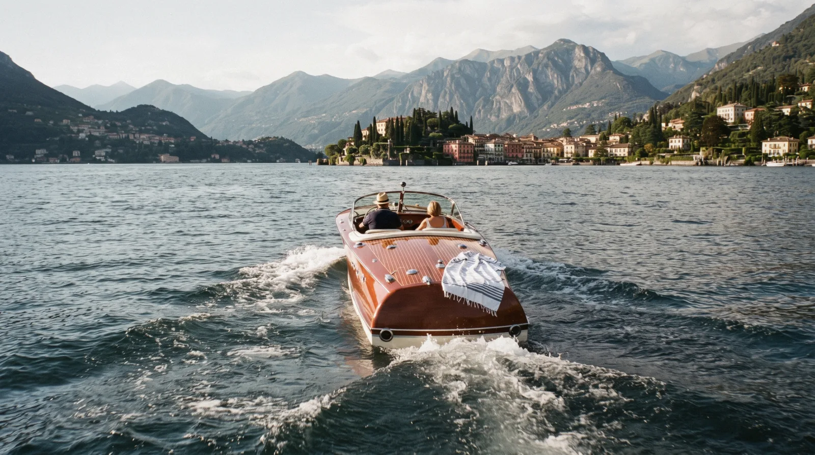 A varnished wooden launch crossing open water below the western shore, on a Lake Como boat tour